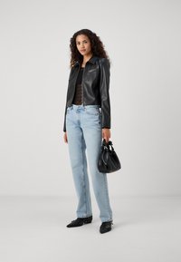 Giacca di pelle nera con un design leggermente accorciato, abbinata a un top in pizzo nero, jeans dritti blu chiaro e una borsa nera.