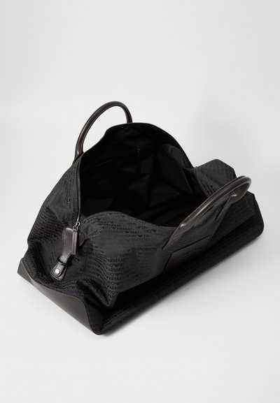 Grand sac de sport noir avec un extérieur texturé et un motif de logo répétitif, des poignées doubles et un intérieur spacieux non doublé.