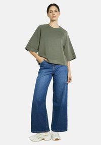 Sweatshirt oversized vert olive à manches courtes, associé à un jean clair à jambes larges. Des baskets blanches viennent compléter le look.