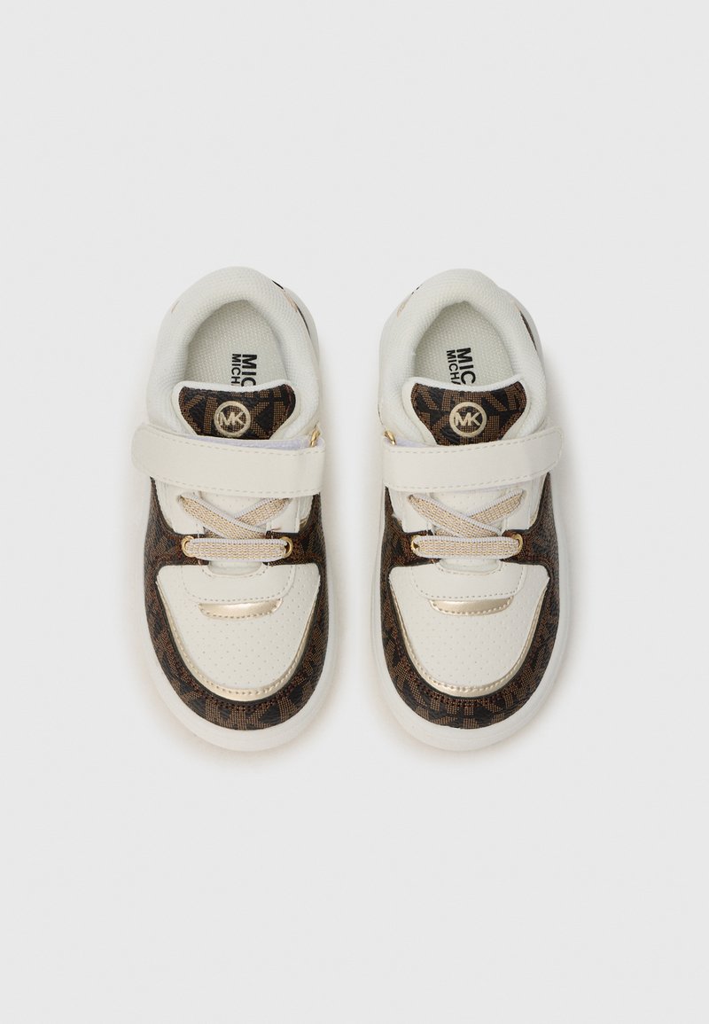 Baskets blanches avec des panneaux latéraux à motifs marron, dotées d'une sangle velcro et de détails en lacets. Des matériaux texturés et des semelles de marque sont visibles.