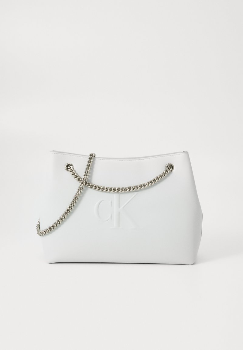 Fehér kézitáska sima anyagból, ezüst láncos vállpánttal és az elején dombornyomott "CK" logóval. Minimalista dizájn, strukturált forma.