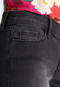 Jeans de mezclilla negra con un diseño ajustado, que presentan un pequeño bolsillo trasero y detalles de costura sutiles. La tela tiene una textura suave.