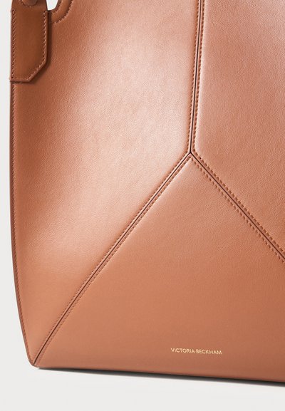 Sac fourre-tout en cuir fauve avec un panneau géométrique cousu et un petit logo doré Victoria Beckham près du bord inférieur.