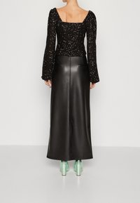 Svart paljetttröja med fyrkantig halsringning och långa ärmar, matchad med en lång svart läderkjol och gröna transparenta klackar.