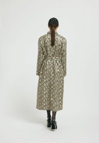 Dolga plašč z beljenjem v zlatem in črnem motivu kače. Ima dolge rokave in gladko teksturo. Nosi se z črnimi čevlji s peto.