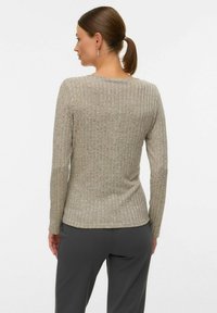 Gaiši bēšs adīts džemperis ar ribota raksta tekstūru, garām piedurknēm un apaļu kakla izgriezumu, redzams no mugurpuses, kopā ar tumši pelēkām biksēm.