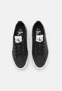 Svarta sneakers i syntetmaterial, med rund tå, snörning, vit sula med text och Calvin Klein-logotyp på tungan.