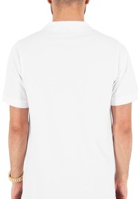 Valge lühikeste varrukatega polo särk klassikalise kraega. Sile tekstuur, puhas disain ilma musterite või aktsentideta. Näidatud tagantvaade.