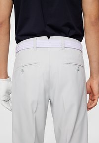 Vaaleanharmaat housut, joissa on teksturoitu valkoinen punottu vyö, varustettuna kahdella takataskulla, joissa on nappikannet. Hansikas käsi näkyy osittain.