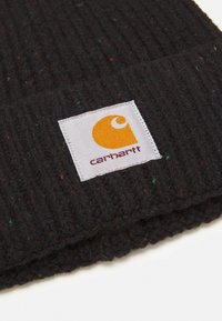 Gorro de punto negro con textura acanalada y pequeña etiqueta blanca con un logo naranja y texto. Presenta motas de color en toda su superficie.