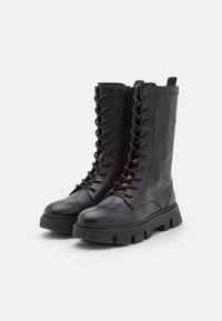 Botines de cuero negro con cordones en el frente, cremallera lateral, suela de goma gruesa y detalles de costura exterior.