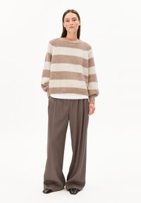 Pull en maille avec des rayures horizontales beige et crème, col rond et coupe ample, associé à un pantalon marron à jambes larges et des chaussures plates.
