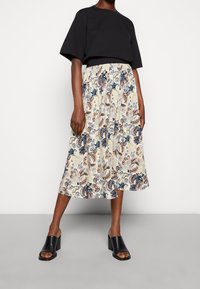 Svart kortärmad topp i kombination med en knälång kjol med blommönster i kräm, blå och röda nyanser. Bärs med svarta klacklåga mules.