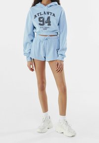 Ljusblå, randig, kort hoodie med grafiken "ATLANTA" och "94"; parat med matchande shorts med dragsko i midjan och sidologotyp.