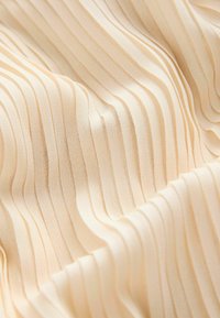 Geplooid stof in een zachte beige kleur, met smalle, gelijkmatig verdeelde verticale ribbels en een gladde, gestructureerde oppervlakte.