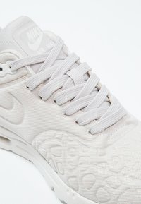 Gros plan sur une basket Nike Air Max blanche avec un tissu texturé, des lacets blancs et un discret logo Nike embossé sur le côté.