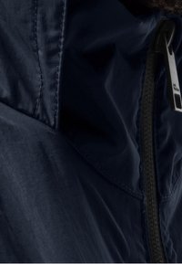 Námorní větrovka s ripstop texturou, vysokým límcem, černým zipem a subtilním prošitím. Lehká a odolná vůči povětrnostním vlivům.