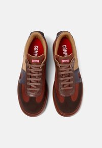 Braune und rostfarbene Sneakers aus Mesh- und Wildledermaterialien. Sie verfügen über eine abgerundete Zehenpartie, Schnürsenkel und ein rotes Innenfutter mit einem Markenetikett.