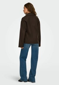 Bruine, oversized jas met een kraag en lange mouwen, gecombineerd met blauwe wijde spijkerbroeken. Gladde textuur, minimale hardwaredetails.