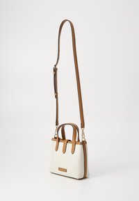 White canvas bag with brown leather handles and strap. Features side accents and a rectangular shape. Gold hardware attached to strap.