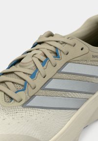 Αθλητικό παπούτσι μπεζ με υφή στην επιφάνεια, διαθέτει γκρι πλαϊνές ρίγες, μπλε λεπτομέρειες στα κορδόνια και μαλακή σόλα.
