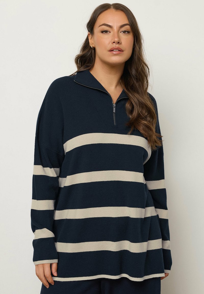 Pullover navy con design a righe crema, dotato di colletto con zip quarti e vestibilità ampia. Il morbido tessuto a maglia offre una texture confortevole.