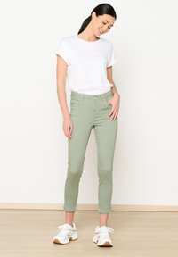 Heledad rohelised skinny-jeansid kõrge vöökohaga, millel on vöökohaga aasad, esipocketid ja pehme kangatextuur, koos valge T-särgi ja spordikingadega.