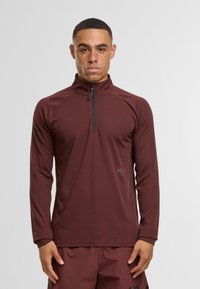 Bordeauxfarbener Quarter-Zip-Pullover mit langen Ärmeln, strukturiertem Stoff und einem schwarzen Reißverschluss. Mit dezentem Logo auf der linken Seite.