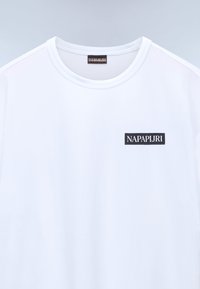 Hvid kortærmet t-shirt med rund hals, udstyret med et sort rektangulært logo patch med "NAPAPIJRI" på venstre brystområde.