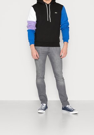 Felpa con cappuccio nera con maniche bianche, viola e blu. Abbinata a jeans grigi e sneakers blu navy. Presenta un piccolo logo sul petto.