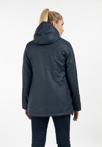 Giacca impermeabile blu navy con cappuccio, texture liscia e orlo leggermente più lungo, caratterizzata da un design minimalista e senza hardware visibile.