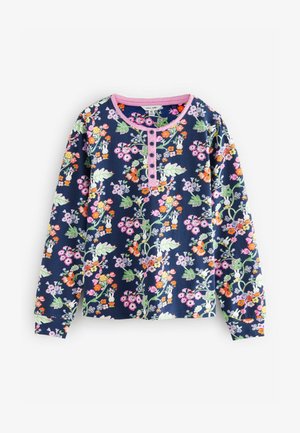 Tumesinise pikkade varrukatega pluus, millel on mitmevärvilised lille- ja jänesemustrid, ümmargune kaelus ja nelja nööbiga nööpiring roosa äärisega.