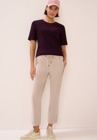 Chemise violette à manches courtes associée à un pantalon beige à cordon. Les chaussures sont des baskets de couleur claire. Design simple avec coupe décontractée et poches.