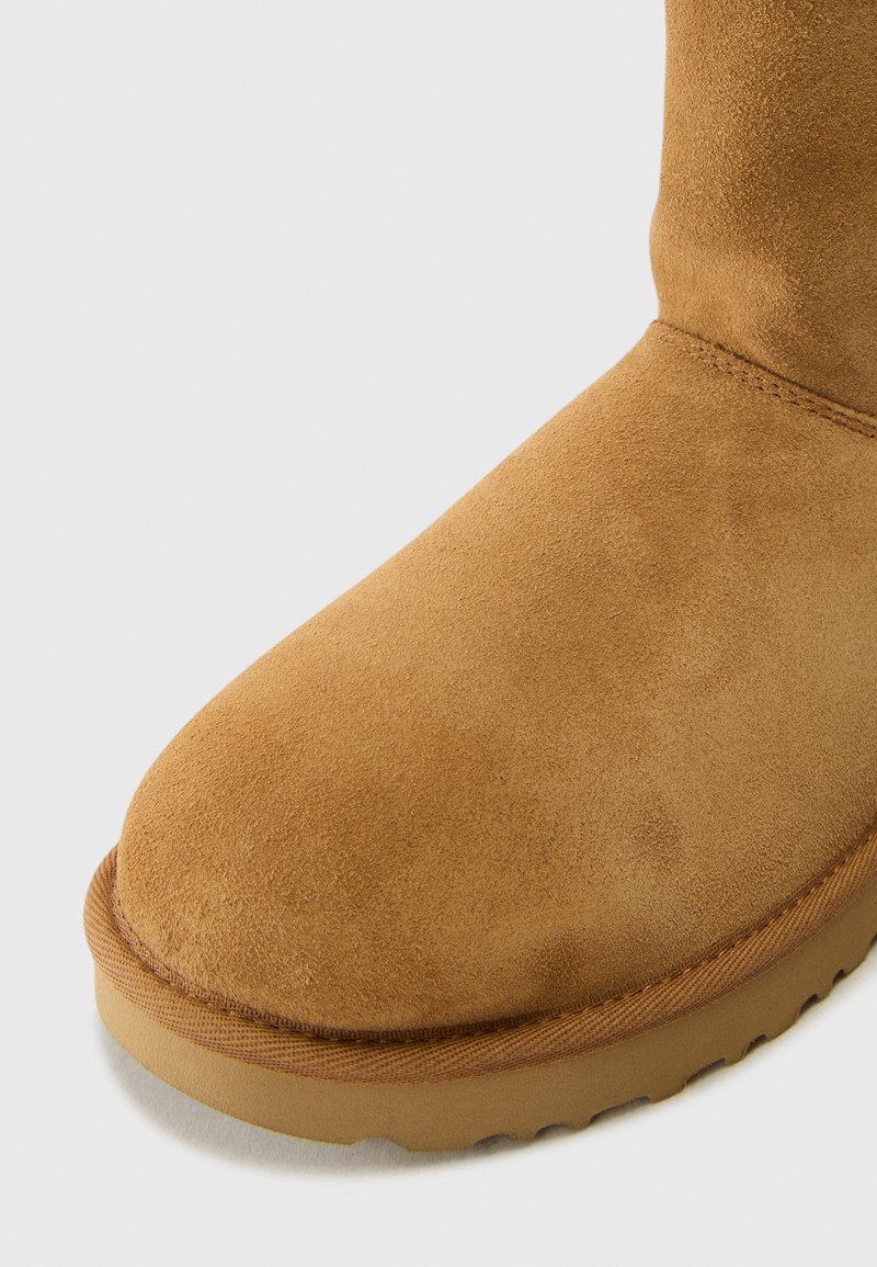 Beige Wildlederschuh mit runder Zehenform und weicher Textur, ausgestattet mit einer hellbraunen Gummisohle und gestickten Details entlang der Naht.