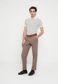 Ριγέ πόλο με κοντά μανίκια σε λευκό και ναυτικό μπλε, καφέ ραμμένα παντελόνια, καφέ ζώνη και μαύρα μοκασίνια. Λείο ύφασμα με εφαρμοστή σχεδίαση.