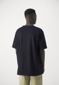 Schwarzes Baumwoll-T-Shirt mit klassischem Rundhalsausschnitt, kurzen Ärmeln und lockerer Passform, von hinten dargestellt. Keine sichtbaren Logos oder Muster.