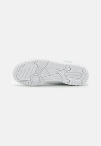 Weiße Sportlich Sneaker-Sohle mit tiefen Profilmustern und Rillen, mit einem runden Logo in der Mitte und dem Text "New Balance".