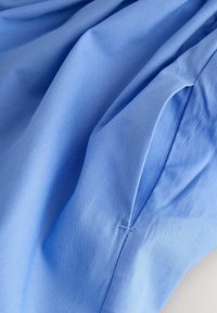 Tessuto azzurro chiaro con una texture liscia, che mostra morbidi pieghe e drappeggi. Presenta un sottile dettaglio cucito vicino al bordo.