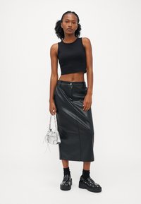 Top scurt negru, fustă midi din piele ecologică neagră, geantă transparentă, pantofi cu platformă negri cu studs și șosete negre până la gleznă. Design simplu.