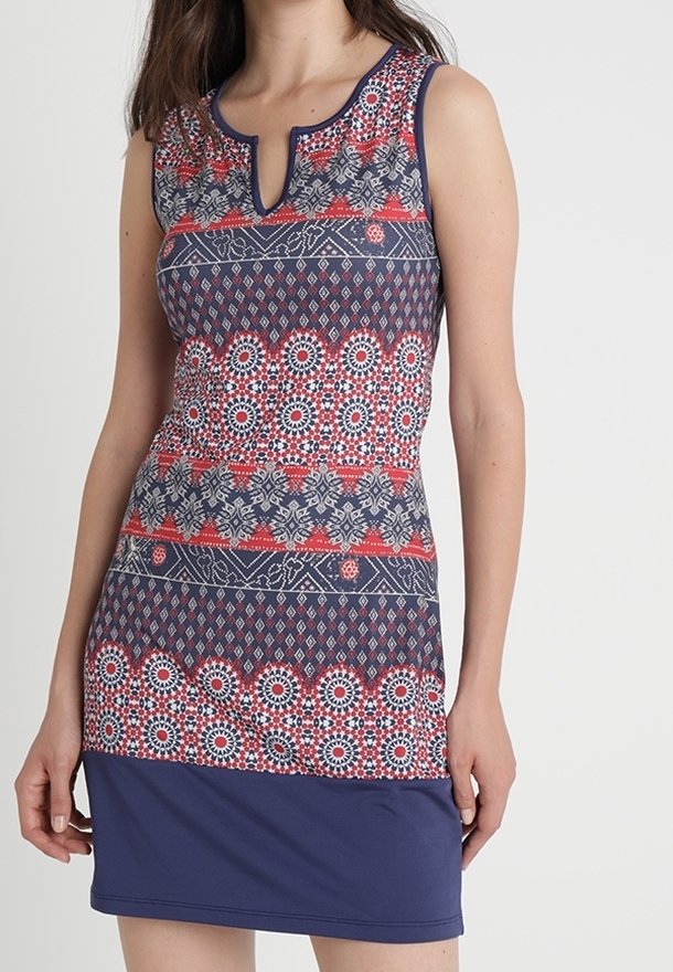 Femme portant une robe sans manches avec des motifs géométriques et floraux bleus marine, rouges et blancs, avec une petite fente en V au niveau du décolleté.