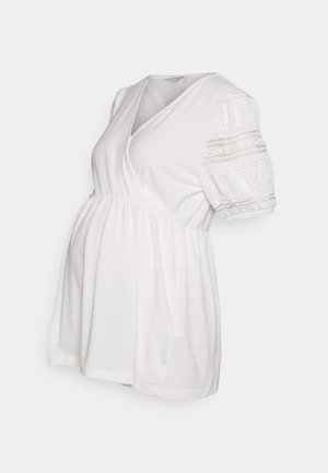 Biała bluzka ciążowa z dekoltem w serek, krótkimi bufkami z koronkowymi detalami i cinchowanym w pasie dla luźniejszego dopasowania. Wykonana z miękkiej bawełny.