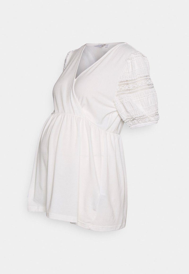 Bílý těhotenský top s výstřihem do V, krátkými nadýchanými rukávy s krajkovými detaily a staženým pasem pro uvolněný střih. Měkká bavlněná tkanina.