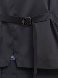 Crni kaput s pojasom, glatke teksture, s metalnom kopčom. Dizajn uključuje urezanu pozadinu i slojeviti kroj.