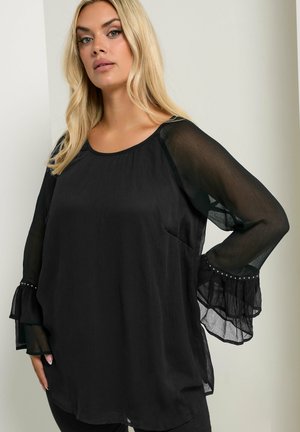 Zwarte blouse met doorzichtige lange mouwen en gerimpelde manchetten. Heeft een ontspannen pasvorm en subtiele kraalaccenten op de mouwzoom. Soepele textuur.