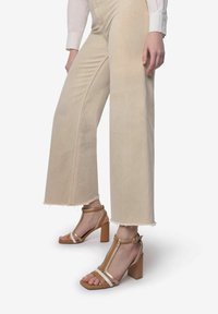 Beige brede jeans med frynset kanter, parret med lysebrune blokkede hælesandaler med stropper og en tæppe-design.