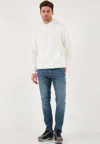 Hvid hættetrøje med frontlomme, kombineret med blå jeans og afslappede sneakers med grå og marineblå detaljer.