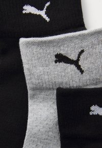 Chaussettes tricotées noires et grises avec un tissu texturé. Chaque chaussette présente un logo Puma contrastant en blanc, mettant en valeur un design simple.