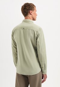 Lichtgroen overhemd met lange mouwen, een button-down kraag, gestoffeerd materiaal en een afgeronde zoom. Bevat een enkele sluitingdetail op de achterkant.