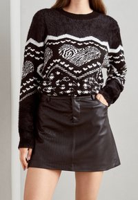 Schwarz-weißer gemusterter Pullover mit flauschiger Textur, kombiniert mit einem schwarzen Fake-Leder-Minirock mit vertikalen Streifen und seitlichen Taschen.