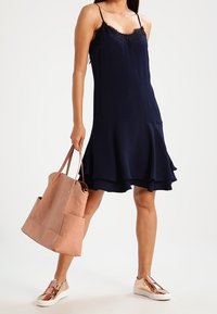 Mörkblå ärmlös klänning med spetsdetaljer och utsvängd nederkant. Kombinerad med en ljusrosa tote-väska och roseguld sneakers för en avslappnad look.